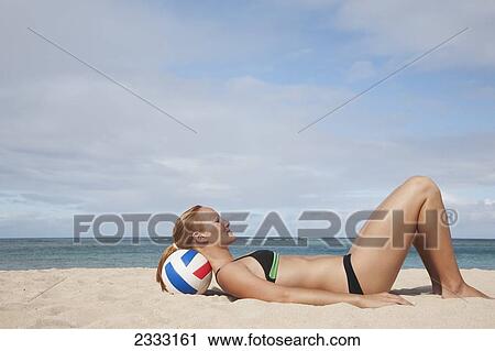 A girl in a two piece bathing suit laying on the sand resting her head on a volleyball; Waikiki, Hawaii, United States of America View Large Photo Image Stock Image - A girl in a two piece bathing suit laying on the sand resting her head on a volleyball; Waikiki, Hawaii, United States of America. Fotosearch