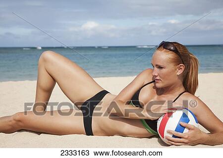 Stock Image - A girl in a two piece bathing suit laying on the sand with a volleyball; Waikiki, Hawaii, United States of America. Fotosearch