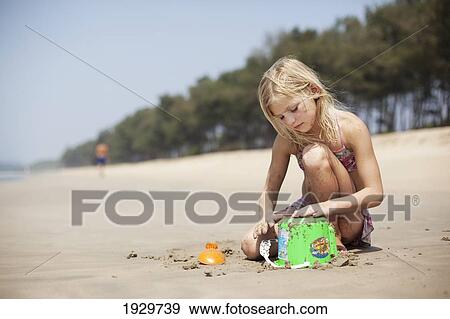 Stock Photo - A girl makes sandcastles with a green bucket on Turtle Beach, Goa, India.. Fotosearch