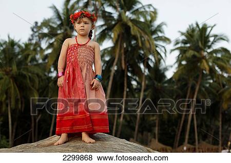 Stock Photo - A girl on a rock in a red dress with flowers in her hair, Patnum beach, Goa, India.. Fotosearch