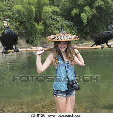 A Girl Poses With A Unique Hat And A Stick Holding Two Birds Along A River; Guilin, Guangxi, China View Large Photo Image Stock Photograph - A Girl Poses With A Unique Hat And A Stick Holding Two Birds Along A River; Guilin, Guangxi, China. Fotosearch