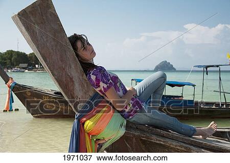 Stock Photo - A Girl Relaxes On A Boat On The Shore; Phi Phi Islands Thailand. Fotosearch