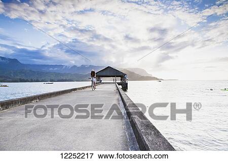 A girl rides her bike down the famous pier at sunset in Hanalei Bay; Kauai, Hawaii, United States of America View Large Photo Image Stock Photo - A girl rides her bike down the famous pier at sunset in Hanalei Bay; Kauai, Hawaii, United States of America. Fotosearch
