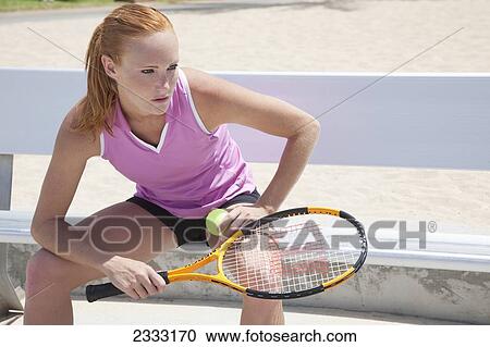 Stock Image - A girl sitting on a bench with a tennis ball and racquet; Oahu, Hawaii, United States of America. Fotosearch