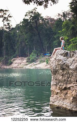 Stock Photography - A girl waits to jump from this cliff and swim outside the Seven kilometre caves; Kong Lor, Laos. Fotosearch