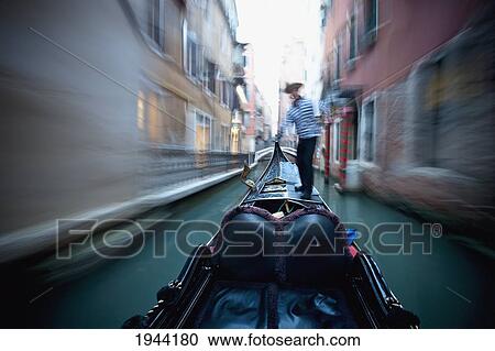 Stock Image - A Gondolier Rowing A Gondola Through A Canal; Venice Venezia Italy. Fotosearch