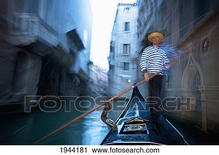 Stock Image - A Gondolier Rowing A Gondola Through A Canal; Venice Venezia Italy. Fotosearch