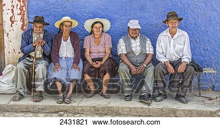 Stock Image - A group of elderly Bolivian people sit on a bench watching a basketball game on a hot afternoon; Bolivia. Fotosearch