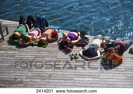 A group of people laying on a wooden dock at the water's edge in the warm sunshine; Barcelona, Spain View Large Photo Image Stock Image - A group of people laying on a wooden dock at the water's edge in the warm sunshine; Barcelona, Spain. Fotosearch