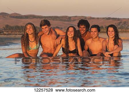 Stock Photo - A group of teenagers in bathing suits sitting in water at sunset; Tarifa, Cadiz, Andalusia, Spain. Fotosearch
