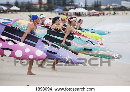 Picture - A Group Of Women Running From The Shore Into The Water Holding Their Surfboards; Tarifa, Cadiz, Andalusia, Spain. Fotosearch
