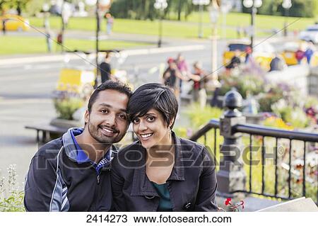 Stock Image - A happy young Indian ethnicity couple sit together; Victoria, Vancouver Island, British Columbia. Fotosearch