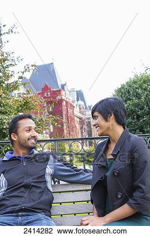 A happy young Indian ethnicity couple sit together on a park bench; Victoria, Vancouver Island, British Columbia View Large Photo Image Stock Image - A happy young Indian ethnicity couple sit together on a park bench; Victoria, Vancouver Island, British Columbia. Fotosearch