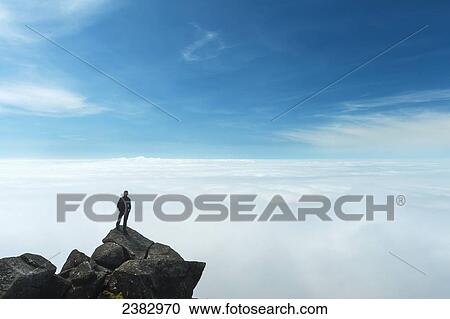 Stock Image - A hiker admiring the view from the top of Sgurr nan Eag, one of the peaks in the Black Cuillin; Isle of Skye, Scotland. Fotosearch