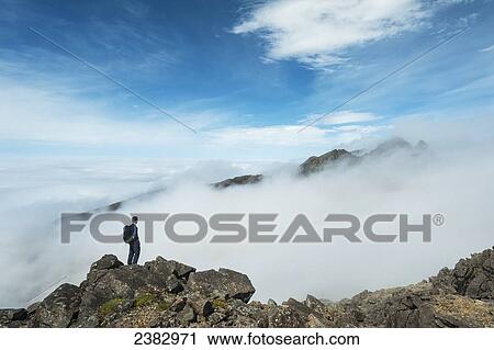 Stock Image - A hiker admiring the view from the top of Sgurr nan Eag, one of the peaks in the Black Cuillin; Isle of Skye, Scotland. Fotosearch
