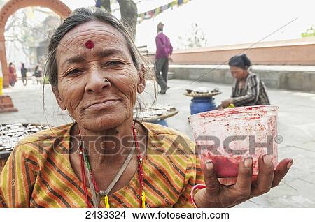 Picture - A Hindu woman in Swayambhu temple painting thirth eye to the tevotees; Kathmandu, Nepal. Fotosearch