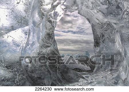 Stock Image - A hole in a coastal iceberg by the atlantic ocean with other icebergs seen through it; iceland. Fotosearch