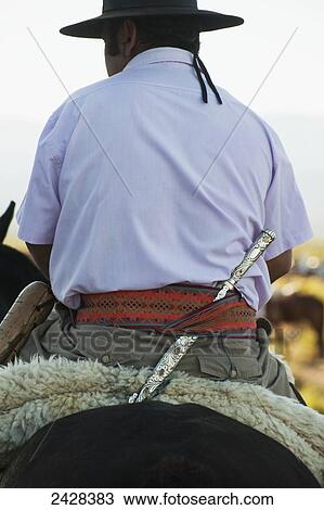 Stock Image - A horse and rider with a knife tucked into his belt; Malargue, Argentina. Fotosearch