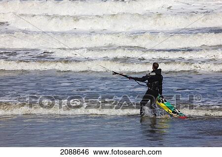 Stock Photograph - A Kitesurfer Stands Watching The Waves Come In; Tynemouth Tyne And Wear England. Fotosearch