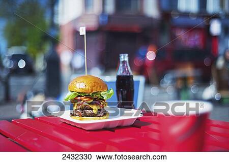 Stock Image - A large hamburger and bottle of pop on a table; London, England. Fotosearch