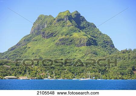Stock Photo - A Large Rock Formation Against A Blue Sky Along The Coast; Bora Bora Society Islands French Polynesia South Pacific. Fotosearch