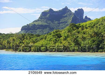 Stock Photo - A Large Rock Formation Against A Blue Sky Along The Coast; Bora Bora Society Islands French Polynesia South Pacific. Fotosearch