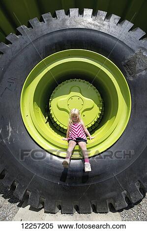 Stock Photography - A little girl sits on the tire of The World's Largest Truck; Sparwood, British Columbia, Canada. Fotosearch