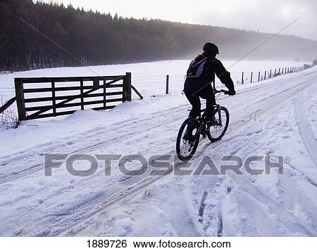 Stock Photograph - A Lone Cyclist Riding On A Snowy Rural Road. Fotosearch