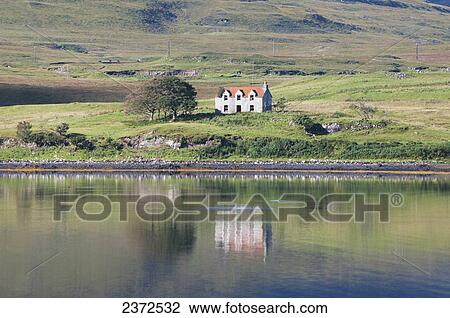 Stock Image - A lone house along the shoreline of the water; Skye, Scotland. Fotosearch