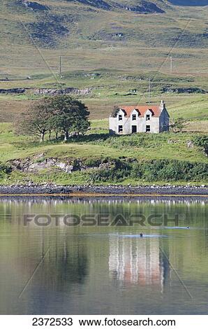 Stock Image - A lone house along the shoreline of the water; Skye, Scotland. Fotosearch