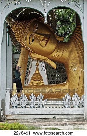 Stock Image - A male tourist takes a photograph of the large reclining Buddha. Wat Somdet; Sangkhlaburi, Kanchanaburi, Thailand. Fotosearch