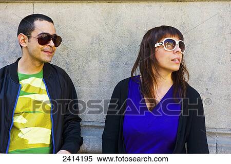 Stock Photography - A man and woman in sunglasses standing against a concrete wall; Barcelona, Spain. Fotosearch