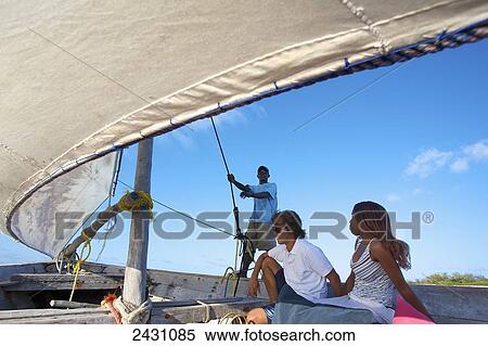 A man and woman sit onboard a sailboat as a man holds the sail; Vamizi Island, Mozambique View Large Photo Image Stock Photography - A man and woman sit onboard a sailboat as a man holds the sail; Vamizi Island, Mozambique. Fotosearch