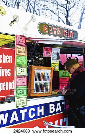 Stock Image - A man at a stand for getting keys cut and watch sale and repairs, Portobello Market; London, England. Fotosearch