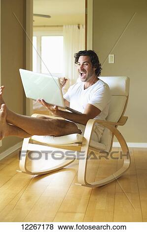 Stock Photo - A man celebrating at what he reads on his laptop computer; Wailua, Kauai, Hawaii, United States of America. Fotosearch