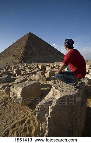 Stock Image - A Man Crouching Near A Pyramid In The Desert. Fotosearch