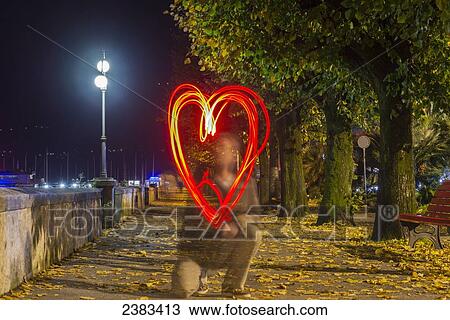 Stock Image - A man drawing a red glowing heart shape in the air; Locarno, Ticino, Switzerland. Fotosearch