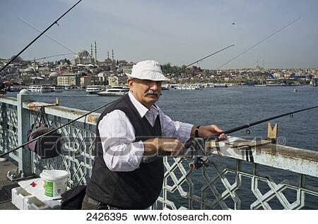 Stock Photography - A man fishes off a bridge; Istanbul, Turkey. Fotosearch