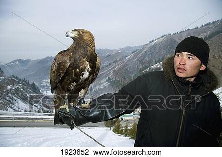 Stock Image - A Man Holding An Eagle On His Arm, Posing For Tourist Photos At A Tourist Spot In The Mountains Around Almaty, Almaty, Kazakhstan. Fotosearch