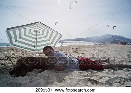 A Man Laying On Punta Paloma Beach With His Dog Under An Umbrella; Tarifa Cadiz Andalusia Spain View Large Photo Image Stock Photo - A Man Laying On Punta Paloma Beach With His Dog Under An Umbrella; Tarifa Cadiz Andalusia Spain. Fotosearch