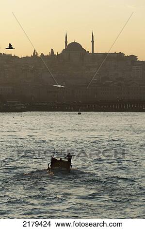 A Man On A Boat In The Water With The Suleymaniye Mosque In The Background At Sunset; Istanbul Turkey View Large Photo Image Picture - A Man On A Boat In The Water With The Suleymaniye Mosque In The Background At Sunset; Istanbul Turkey. Fotosearch