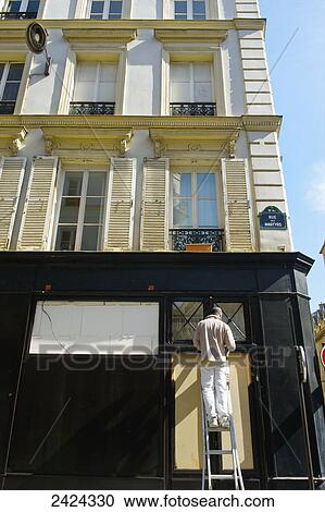 Stock Image - A man on a ladder repairing the exterior of a residential building; Paris, France. Fotosearch