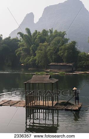 Stock Photo - A Man Paddles Down A River With Mountain Peaks In The Background; Yangshuo, China. Fotosearch