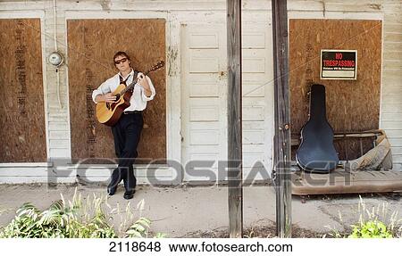 Stock Photo - A Man Plays A Guitar Against A Boarded Up Country Store; Pittsboro North Carolina Usa. Fotosearch