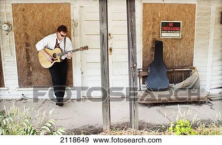 Stock Photo - A Man Plays A Guitar Against A Boarded Up Country Store; Pittsboro North Carolina Usa. Fotosearch
