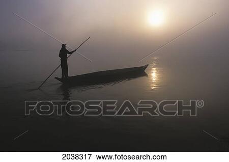 Stock Photo - A Man Pushes His Dugout Canoe Along The Rapti River Near Sauraha And Chitwan National Park At Dawn; Nepal. Fotosearch