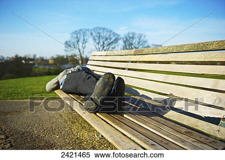 Stock Photography - A man rests on a wooden park bench in Primrose Hill; London, England. Fotosearch