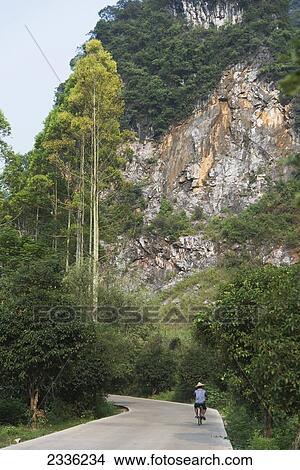A Man Rides A Bicycle Down A Road Beside A Steep Mountainside; Guilin, Guangxi, China View Large Photo Image Picture - A Man Rides A Bicycle Down A Road Beside A Steep Mountainside; Guilin, Guangxi, China. Fotosearch