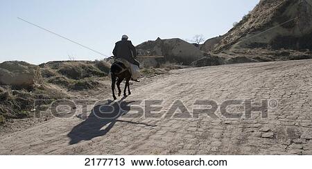 Stock Image - A Man Rides A Horse On A Dirt Road; Ortahisar Nevsehir Turkey. Fotosearch