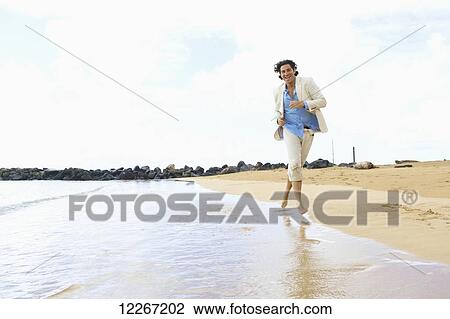 Stock Image - A man runs barefoot in the surf on Lydgate Beach; Kauai, Hawaii, United States of America. Fotosearch